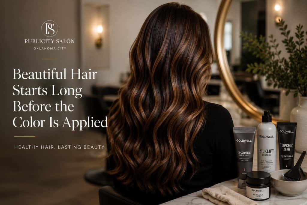 Woman with healthy, glossy brunette balayage hair in a salon chair, with Goldwell color products on the counter at Publicity Salon Oklahoma City